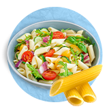 Primer plano de un tazón blanco con ensalada de pasta y ziti sueltos delante del tazón sobre un fondo azul.