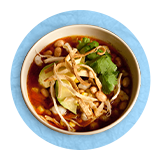 Plano aéreo de un tazón de sopa de tortilla sobre un fondo azul.