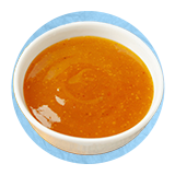 Primer plano de un tazón blanco lleno de aderezo de ensalada sobre un fondo azul.