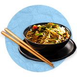 Lo Mein noodles in a black bowl on top of a black plate with chopsticks, on a blue background.