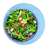 Plano aéreo de un tazón azul con ensalada de hojas verdes sobre un fondo azul.