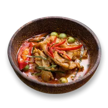 A bowl of spicy Thai seitan curry with green peas, curry seitan strips, and chili peppers.
