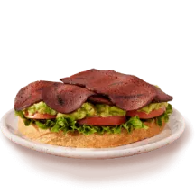 Plant based bacon sandwich with lettuce and tomato on a white dish.