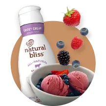 A bottle of natural bliss creamer and a bowl of berries and sorbet on a brown circle.