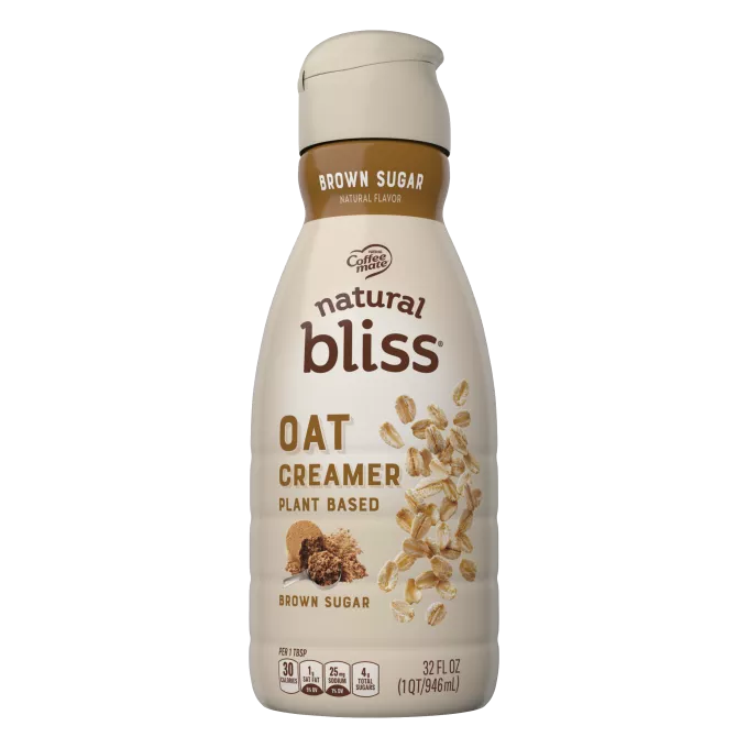 Una botella de creamer Oat Brown Sugar de natural bliss con una etiqueta marrón encima de una taza medidora con azúcar moreno.