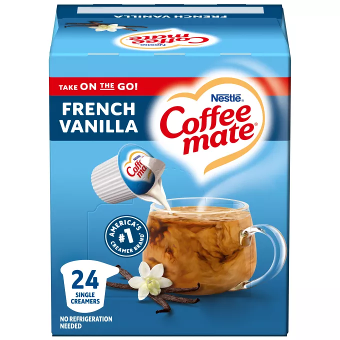 Una caja azul de porciones individuales de creamer Coffee mate Vanilla con una etiqueta azul encima de una taza de café, vaina de vainillas y el logotipo del producto.