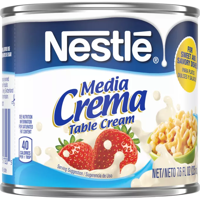 Una lata de crema de mesa que muestra el logo de Nestlé sobre una etiqueta azul con un derrame en color blanco por encima del logo de Media Crema, fresas que caen sobre la crema y la salpican y un tazón de macarrones con queso sobre un remolino azul claro.
