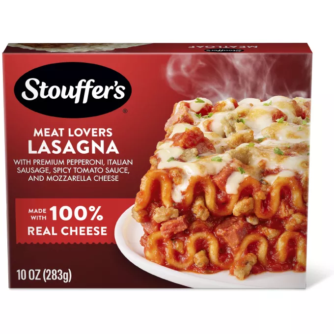 Un plato de Meat Lovers Lasagna sobre una mesa debajo del nombre del producto, el logo de STOUFFER'S y una etiqueta que dice "4 deliciosos tipos de carne".
