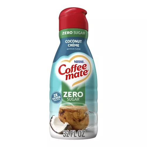 A blue bottle of Zero Sugar Coconut Crème Coffee Creamer with a red cap and green label above a coffee mug and coconut.