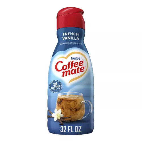 Una botella azul de creamer Coffee mate French Vanilla con una tapa roja y una etiqueta azul sobre una taza de café y vainas de vainilla.