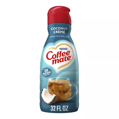 Una botella azul de creamer Coffee mate Coconut Crème con una tapa roja y una etiqueta azul sobre una taza de café y un coco.
