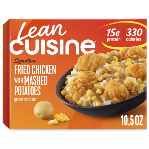 A box of oven fried chicken with mashed potatoes with Protein Kick label with 300 calories, 14 grams of protein and half cup of veggies near a bowl of corn, chicken and potatoes.