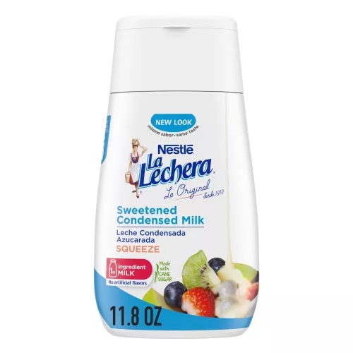 Una botella sirve fácil con una tapa color azul con el logo de La Lechera, junto a una pila de fruta rociada con leche condensada azucarada.