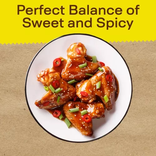 A bottle of Sweet Chili Sauce with a bright red and yellow label and egg rolls beside a cup of sauce.