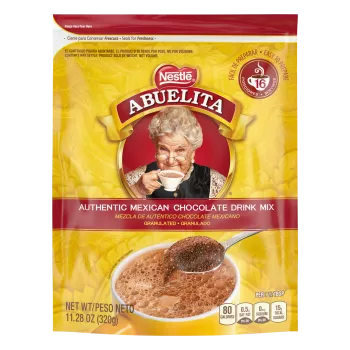 A yellow pouch with red labels and a spoon stirring hot chocolate mix into a yellow mug below the Abuelita logo.