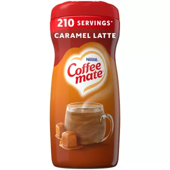 Una lata marrón de creamer Coffee mate Caramel Latte con una etiqueta roja encima de una taza de café con gotas de caramelo.
