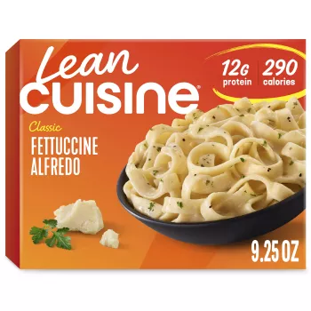 A box of Fettuccini Alfredo with a Comfort Cravings label near a bowl of fettuccini covered with Alfredo sauce.