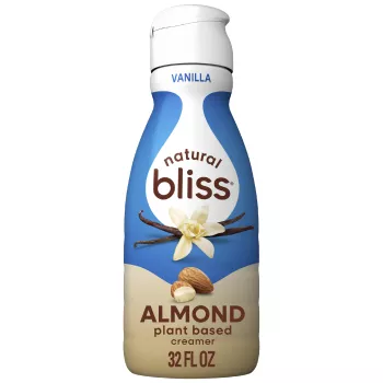 A beige bottle of natural bliss vanilla flavor almond milk creamer with a blue label above vanilla beans and almonds.