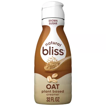 A brown bottle of natural bliss Oat Brown Sugar Creamer with a brown label above a measuring cup of brown sugar.