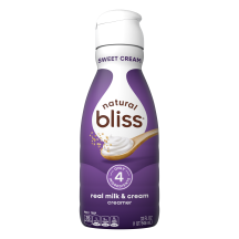 White bottle of natural bliss Sweet Cream flavored Creamer with a purple label above a spoon of sugar and swirl of milk.