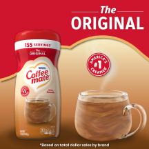 Una lata de creamer en polvo Coffee mate Original con una tapa roja y una etiqueta roja encima de una taza de café y un biscotti.
