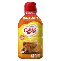 A yellow bottle of Coffee mate Hazelnut Creamer with a red label above a mug of coffee, whole hazelnuts and the product logo.