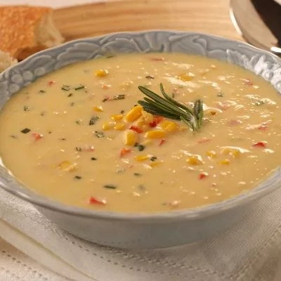 Sopa cremosa de maíz con trozos de pimiento y rama de romero en cuenco azul