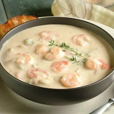 Fotografía de tazón con crema de camarones rosados y ramita de tomillo