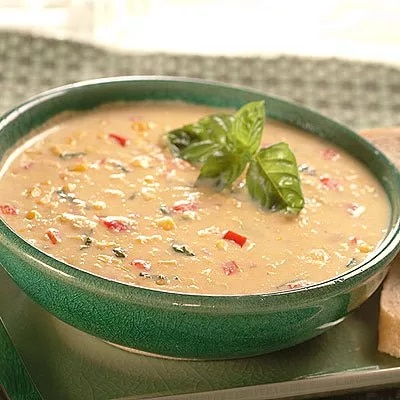 Fotografía de sopa cremosa con trozos de pimiento y albahaca en cuenco verde
