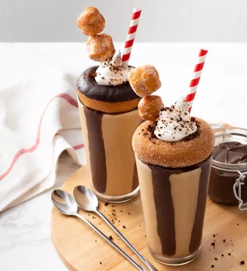 Fotografía de dos batidos de chocolate con crema, pajillas rojas y mini rosquillas