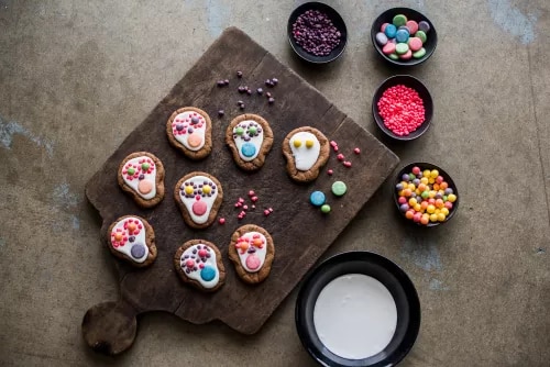 Fotografía de galletas decoradas con caritas, boles de confites y jarra de leche