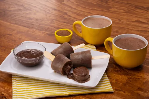 Fotografía de paletas de chocolate en plato, crema de cacao y dos tazas amarillas