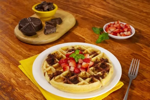 Photo: waffle with chocolate drizzle and diced strawberries on wooden table