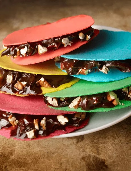 Photograph of colorful cookie sandwich halves filled with chocolate and chopped nuts on a plate