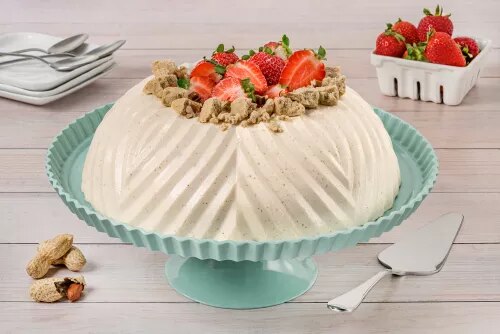 Photograph: white meringue pavlova topped with strawberries and nuts on a pale teal cake stand.