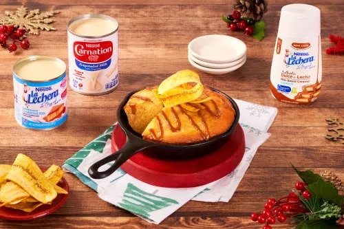Photograph: warm baked bread with orange slices in red skillet, condensed milk cans on wooden table