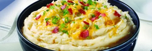 Fotografía: puré de papas cremoso en tazón negro, coronado con cebollín y trozos de tocino