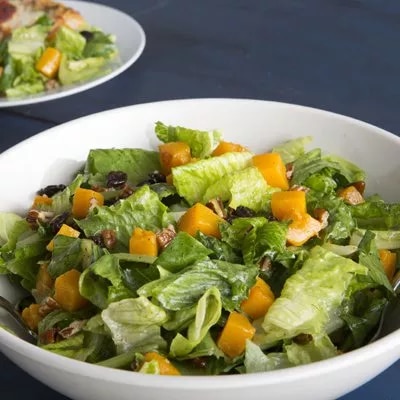 Photograph of a white bowl of green salad with chopped yellow bell pepper on blue cloth