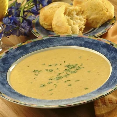 Fotografía: sopa cremosa anaranjada con perejil picado en plato azul y panecillos dorados