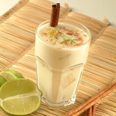 Fotografía de vaso con bebida blanca cremosa, canela en rama y rodajas de lima sobre esterilla