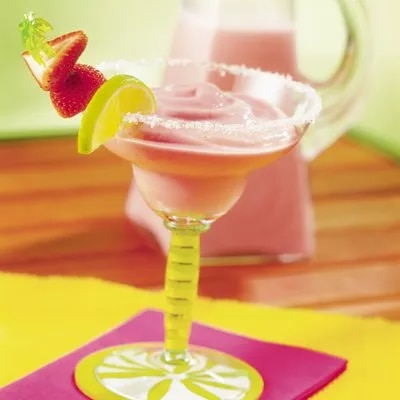 Cóctel rosa en copa margarita con borde salado y guarnición de fresa y lima