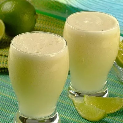 Fotografía: dos vasos con batido cremoso de lima y gajos, sobre tela verde-azul