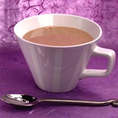 Fotografía: taza blanca con bebida de chocolate sobre tela púrpura y cuchara plateada