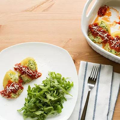 Fotografía de plato con mitades de papa con salsas, rúcula y cuenco sobre mesa