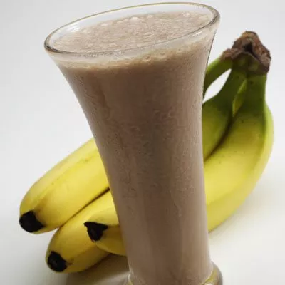Fotografía: batido cremoso de plátano en vaso alto, con racimo de plátanos amarillos