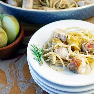 Fotografía de espaguetis cremosos con trozos de pollo y ramita de romero