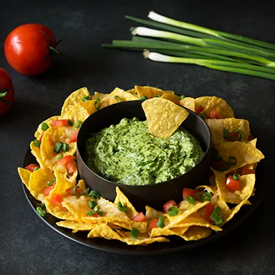 Fotografía: nachos con guacamole en bol, pico de gallo y cebollín sobre fondo oscuro