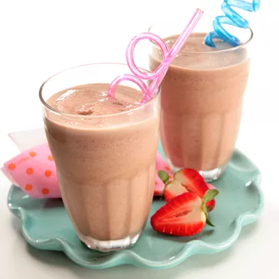 Fotografía: dos batidos rosados en vasos con pajitas, fresas y plato celeste