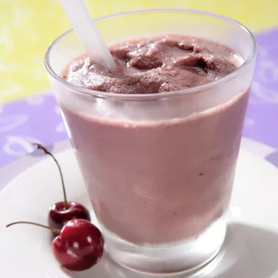 Fotografía: batido cremoso de cereza en vaso con pajita y dos cerezas en plato