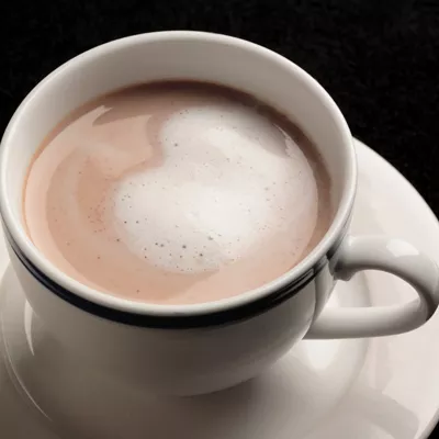 Foto: taza blanca con chocolate caliente y espuma en forma de corazón sobre platillo